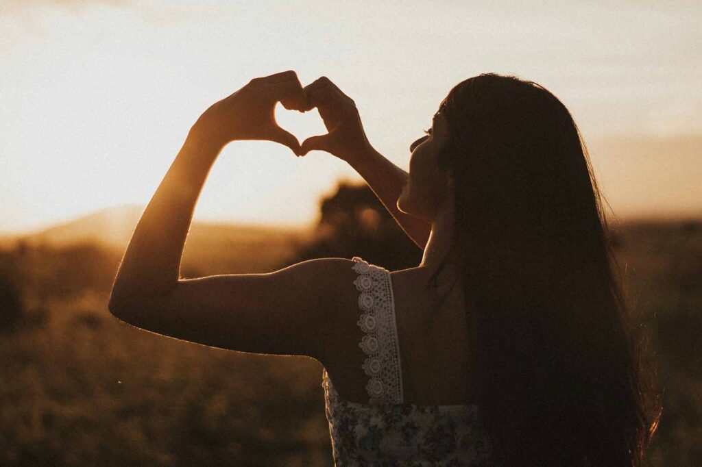 femme épanouie faisant un coeur avec ses mains lors du sunset, gratitude et reconnexion à soi